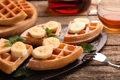 Tasty Belgian waffles with banana and mint on wooden table, closeup