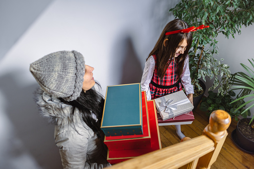 Exciting moment captured as a woman surprises a girl with a stack of beautifully wrapped gifts.