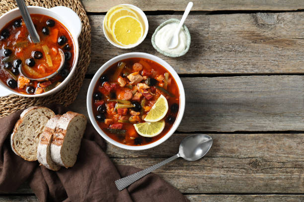 soupe solyanka à la viande avec des saucisses, des olives et des légumes servie sur une table en bois, à plat. espace pour le texte - food heat serving size casserole photos et images de collection