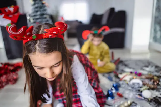 Joyful cooperation between a young brother with a development disability and sister as they eagerly assist in adorning their cozy apartment with Christmas decor.