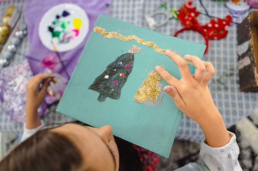 Young girl immersed in crafting a charming Christmas decoration at her workspace.