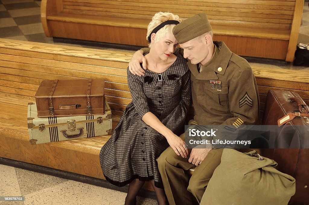 Vintage WWII Bus Station Goodbyes Vintage 1940's US Soldier Saying Goodbye to a Beautiful Woman At A Bus Station.  They are seated on wooden benches with suitcases and a duffel bag. Holding one another.  Patches removed. Leaving Stock Photo