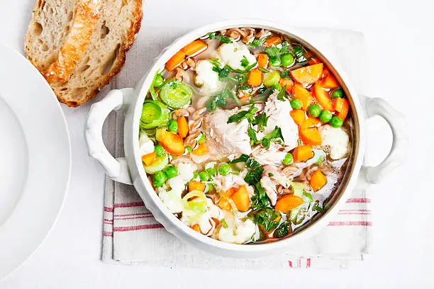 bowl filled with healthy chickensoup, bowl filled with healthy chicken soup, made of chicken, whole wheat pasta, and lots of vegetables, on white tablecloth, with some bread