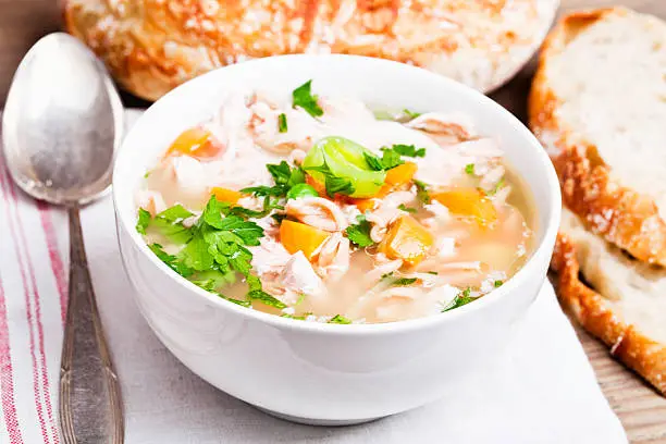 bowl filled with healthy chickensoup, bowl filled with healthy chicken soup, made of chicken, whole wheat pasta, and lots of vegetables, on wooden background, with some bread