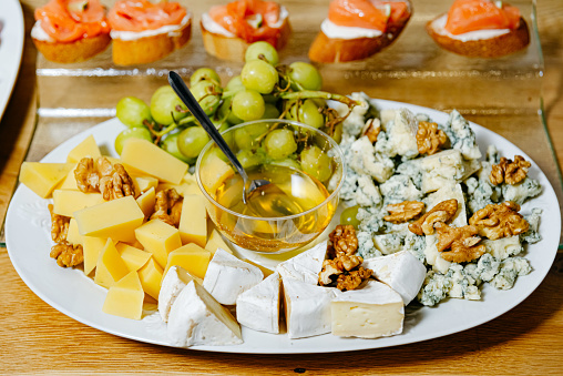 Elegant cheese selection featuring brie, blue cheese, and cheddar, served with honey, walnuts, and green grapes.