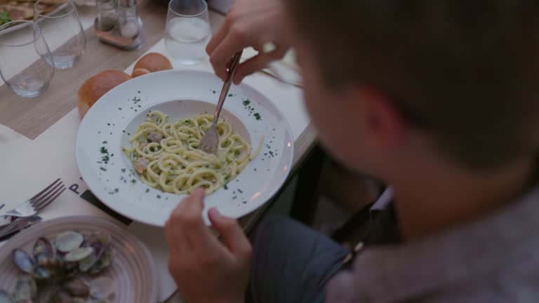 Teenage boy eating sea food spaghetti at an outdoor dining table