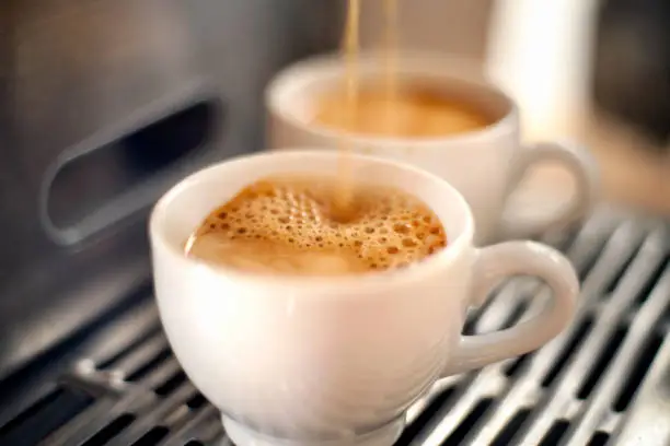 Photo of Two white mugs being filled with espresso