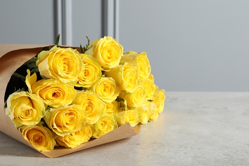 Beautiful bouquet of yellow roses on light grey table, space for text