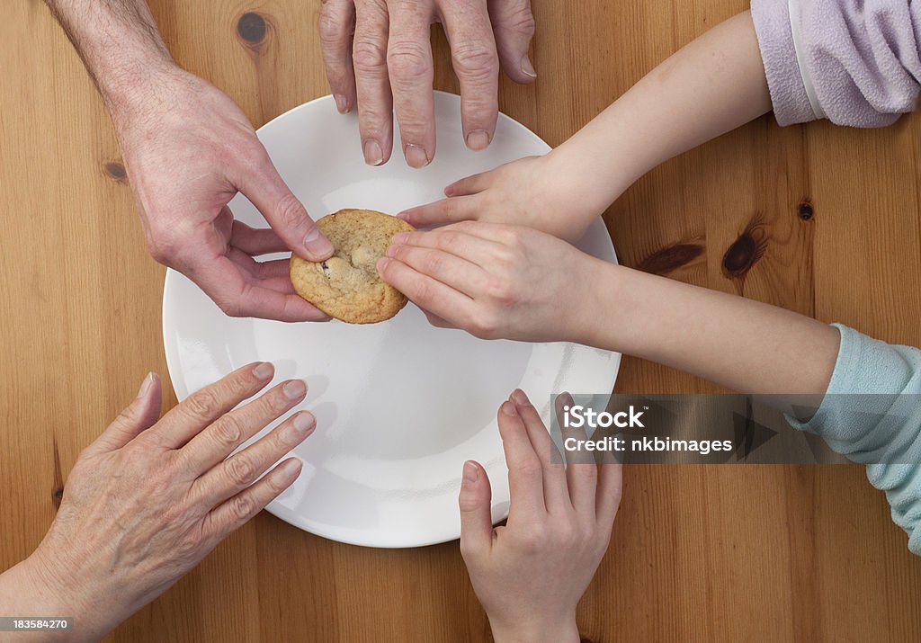 Human greed.  Everyone wants the last cookie. Five hands reach across the plate for the last cookie. Cookie Stock Photo