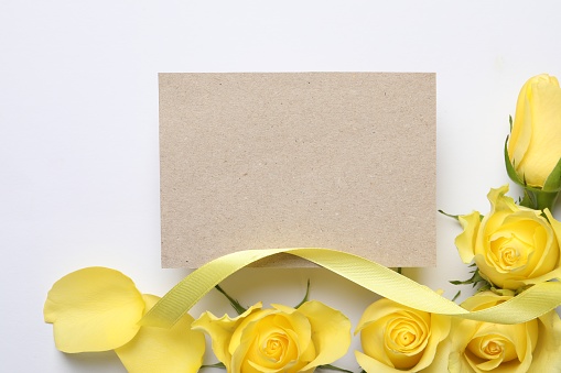 Beautiful yellow roses, petals, ribbon and blank card on white background, flat lay. Space for text