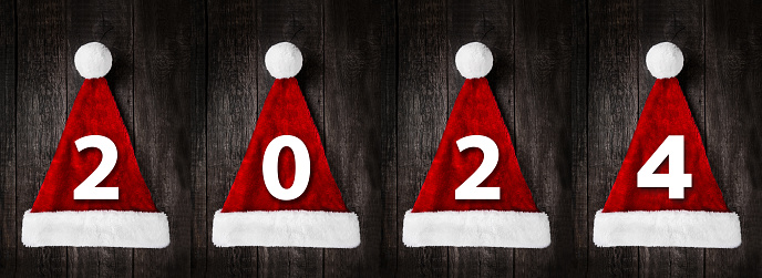 Santa Claus helper hats with sign 2024 on rustic wooden background. Christmas and New Year celebration