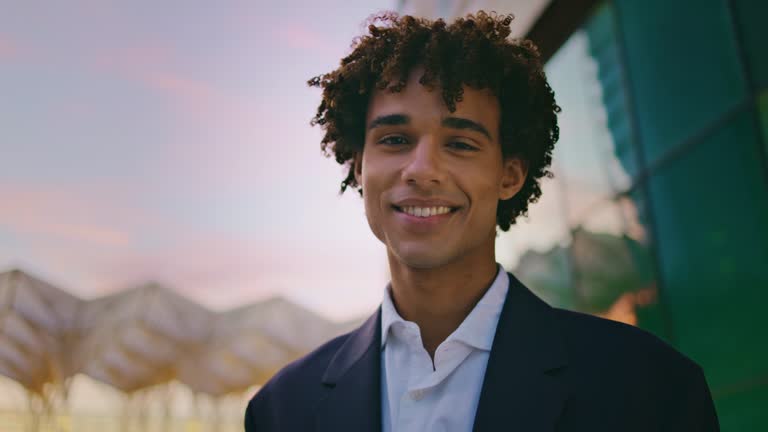 Smiling businessman posing sunset city portrait. Curly young man looking camera