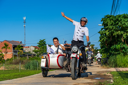 Hoi An, Vietnam - July 07, 2020 : Happy Vietnamese men on classical sidecar motorbike on the street near Old Town of Hoi An, Vietnam