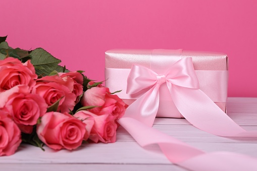 Gift box with pink bow and bouquet of beautiful roses on white wooden table, closeup