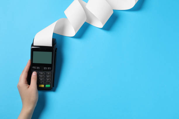 istock Woman using payment terminal with thermal paper for receipt on light blue background, top view. Space for text 1835869789