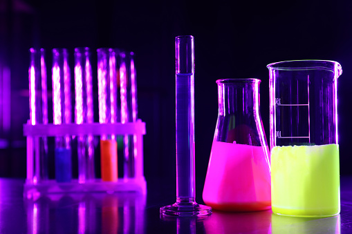 Laboratory glassware with luminous liquids on table against dark background