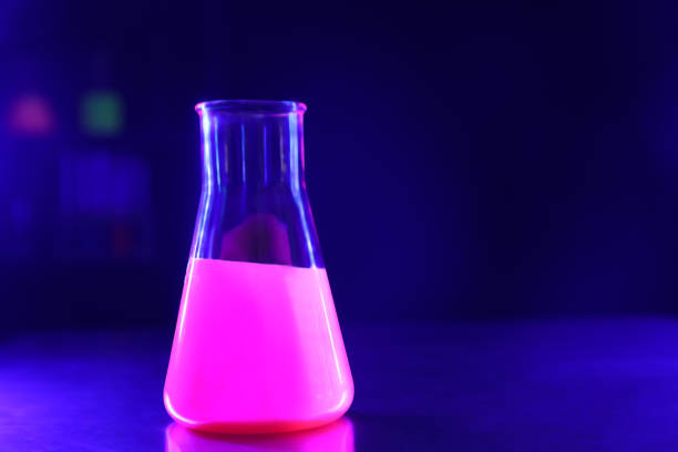 istock Laboratory flask with luminous liquid on table against dark blue background, space for text 1835880473