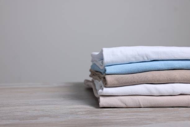 istock Sorting and organizing. Stack of different folded clothes on light wooden table, closeup. Space for text 1835886348