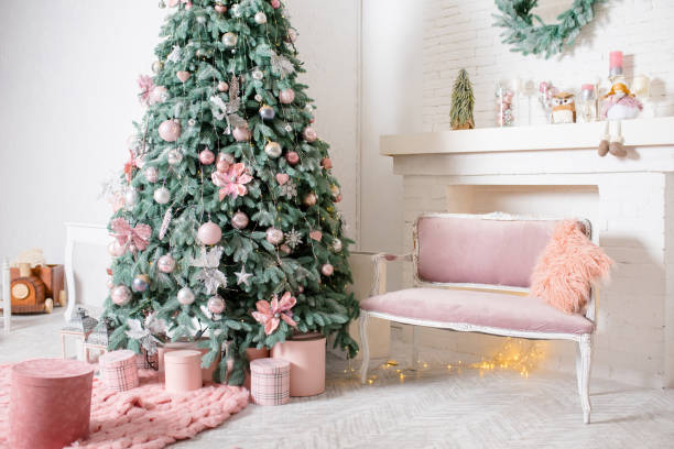 istock New Year's interior design. Lush Christmas tree with pink and silver ornaments. Pink boxes of gifts and a rug, a velour pink sofa with a fluffy pillow. A fireplace with cute Christmas decorations. 1835896594