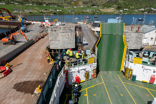 12th May 2023: View from a Caledonian MacBrayne ferry en route to the island of Harris, looking down at the ferry deck and at the Uig commercial port, on the Isle of Skye. The port is a busy ferry terminal that connects the Highlands and islands on the northwest coast of Scotland. Ferry crew are working together to prepare for departure, with the hydraulic gangplank having been raised.