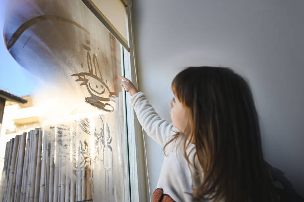 istock Little girl drawing with fingers on window. 1835929412