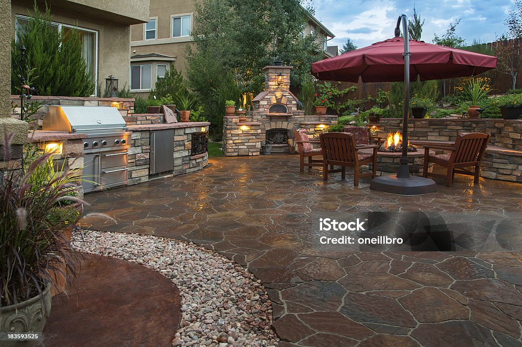 Beautiful Backyard Paver patio with a fire pit, outdoor kitchen, pizza oven and lighting at dusk. Patio Stock Photo