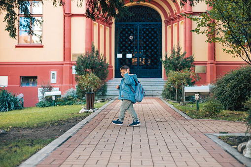 In a watchful moment, the mother stands in front of the school as her son walks in, signifying the beginning of his educational activities for the day
