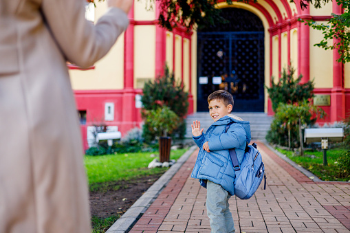 The initiation of the school day unfolds as the son steps inside, with his mother observing in front of the school, marking the beginning of his educational pursuits