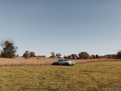 A classic white car sits on the edge of uncut grass, surrounded by a manicured field.