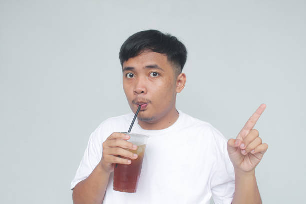 istock Asian young man sucking iced tea and pointing to right with a happy expression. 1835973471