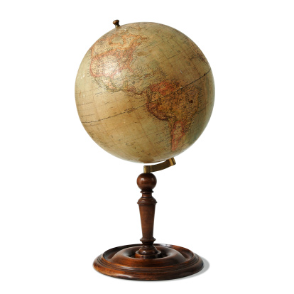 Antique globe, empty parchment, compass and quill standing on the table with library shelves on the background.