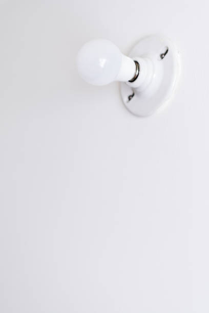 Vertical photo of lamp holder and light bulb on white wall, energy and home spaces theme