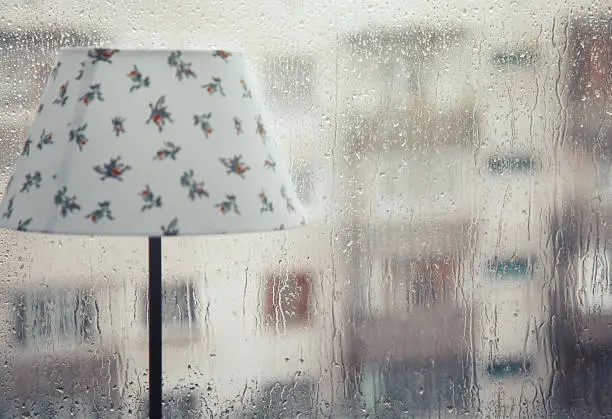 Table lamp at the wet window and rainfall behind the glass