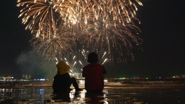 Two kids watch fireworks on the beach at night.