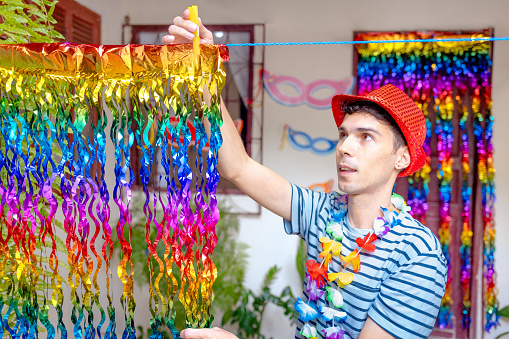 Brazilian man decorates his house with colorful foil curtains for a lively Carnival party. Perfect for reflecting the joyful joy of Carnival celebrations.