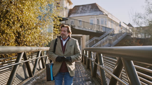 SLO MO Mature Businessman with Shoulder Bag Using Smartphone While Walking on Pedestrian Bridge Over River in Graz City