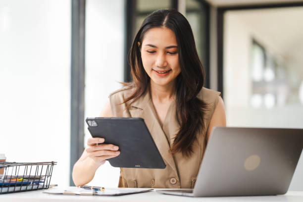 istock Asian freelance writer takes notes at her desk with a laptop in a bright, modern office setting 1836164112