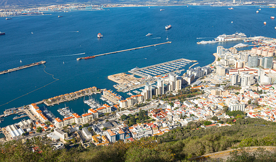 Gibraltar - 11th November 2023: Elevated view of part of the western seaboard of the Gibraltar featuring Midtown Marina, Queensway Quay Marina, The Island, breakwaters, the Port of Gibraltar, Gibraltar Bay with tankers and other ships, and looking over towards Algeciras in Spain.