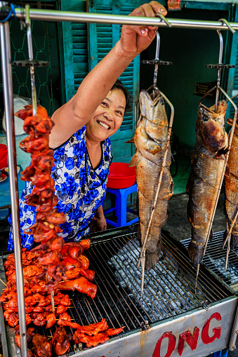 Vietnamese woman preparing grilled frogs and fishe, Mekong River Delta, Vietnam