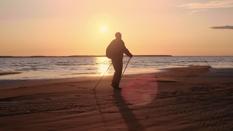 Mature man silhouette Scandinavian walking stick sunset sea sand beach activity healthy lifestyle
