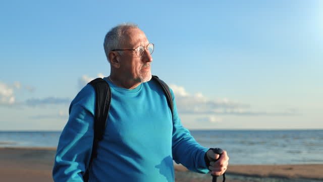 Confident old man Scandinavian walking stick physical activity sunny sea beach sky horizon landscape