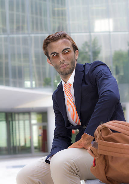 Young vampire businessman outside office with backpack in summer has finished his day work and looking away