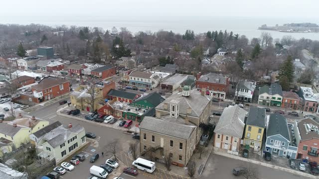 A drone captures an aerial view of Niagara-on-the-Lake's downtown courthouse, slowing zooming out on the surrounding historical buildings on a wintery day while snow lightly falls.