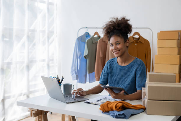 Young African woman selling clothes in streaming video Start a small SME using your smartphone or tablet to receive name orders and ready to ship packages.