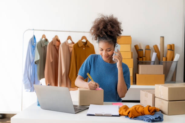 istock Young African woman selling clothes in streaming video Start a small SME using your smartphone or tablet to receive name orders and ready to ship packages. 1836334157