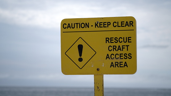 Yellow warning sign about a clear risk to life by being cut off by the rising tide of the North Sea. The beach is deserted due to being mid winter.