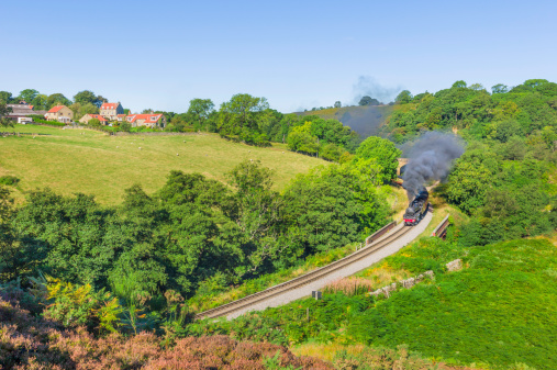 Vintage steam train makes its way through the North York Moors on a bright sunny morning near Goathland, Yorkshire, UK.