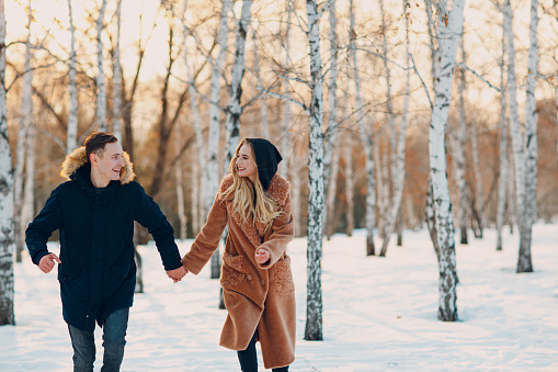 Loving young couple walking playing and having fun in winter forest park.