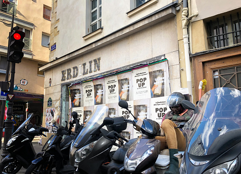 Paris, France: A line of motorcycles parked in front of wall ads in the 3rd arrondissement.