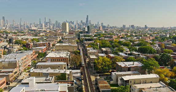 Aerial shot of a subway train in Wicker Park with the downtown Chicago skyline in the background on a clear day in Fall.